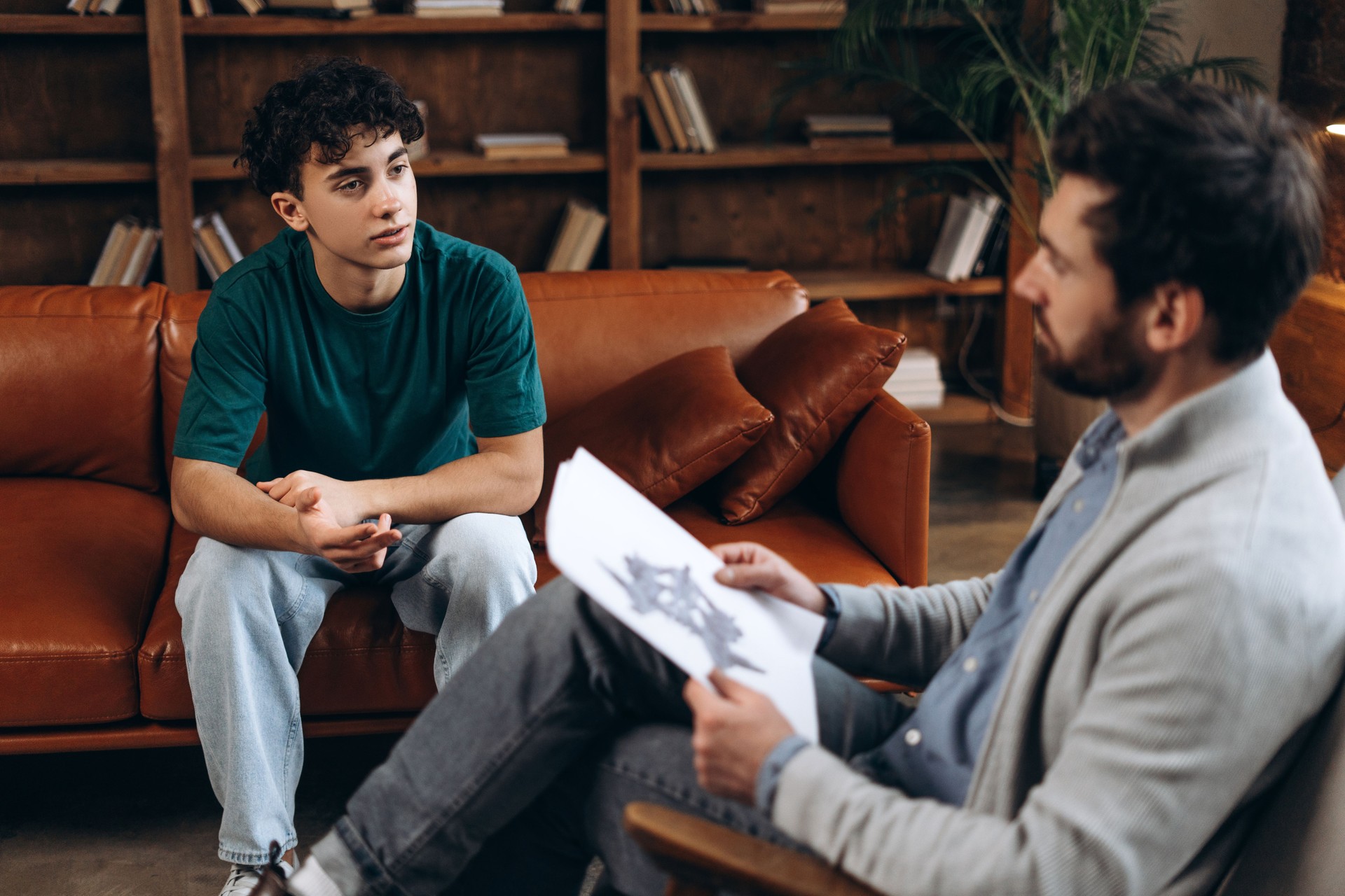 Male therapist consoling upset teenage boy, sitting together in modern office